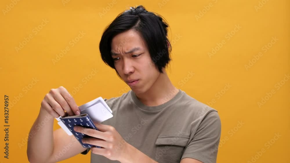 Young angry asian man holding passport and tickets isolated over yellow background Young angry asian man holding passport and tickets isolated over yellow background