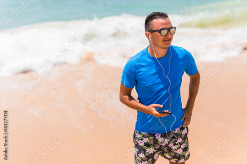 Happy young man enjoying the music on white sandy beach