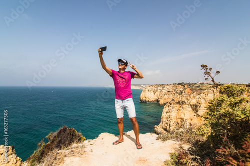 Young man take selfie on the and of the rock near waves of Atlantic ocean