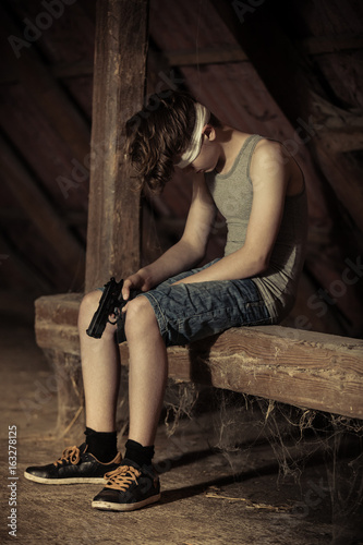 Sad blindfolded child sitting with pistol