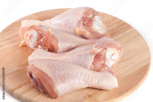 four raw chicken drumsticks on a wooden cutting boardn white background