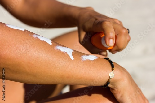 Close up on woman applying sun cream on her arm with a spray at the beach on a warm, sunny day.