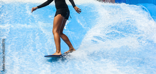 Girl on black swimsuit surfing on wave pool with small board in the island of Phuket, Thailand