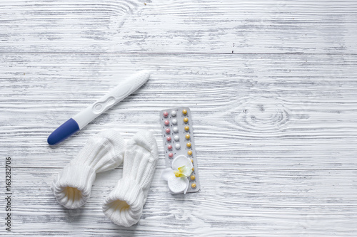 Pregnancy planning. Contraceptive pills  pregnancy test and booties on wooden background top view copyspace