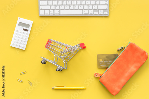 Shopping in online store. Bank card nearby keyboard, purse, shopping cart on yellow background top view