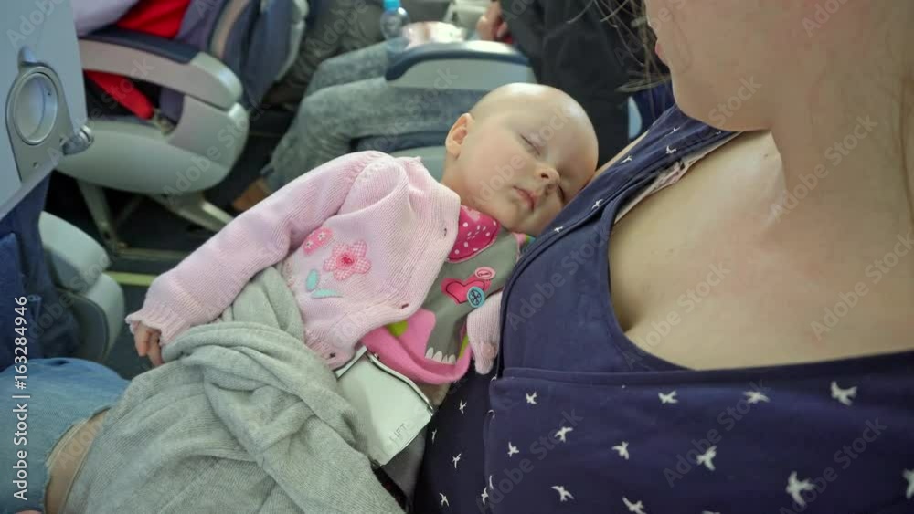A woman holding her child on a plane. The baby is sleeping. Close-up shot