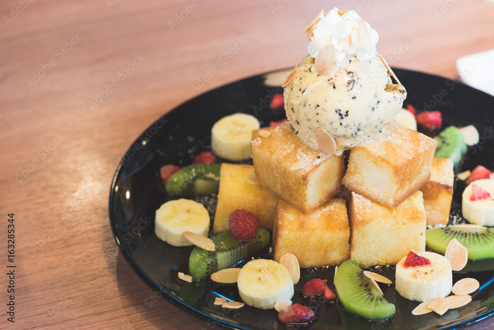 Honey toast wiht mix fruits in the black dish place on the wooden table in the coffee shop in selective focus.