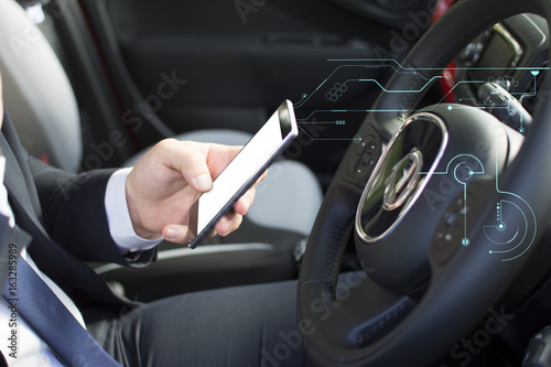 Close-up of a man's hand holding a smartphone. Businessman texting while sitting in a parking lot. Suit and tie man using a mobile phone. Hologram effect. © Addoro