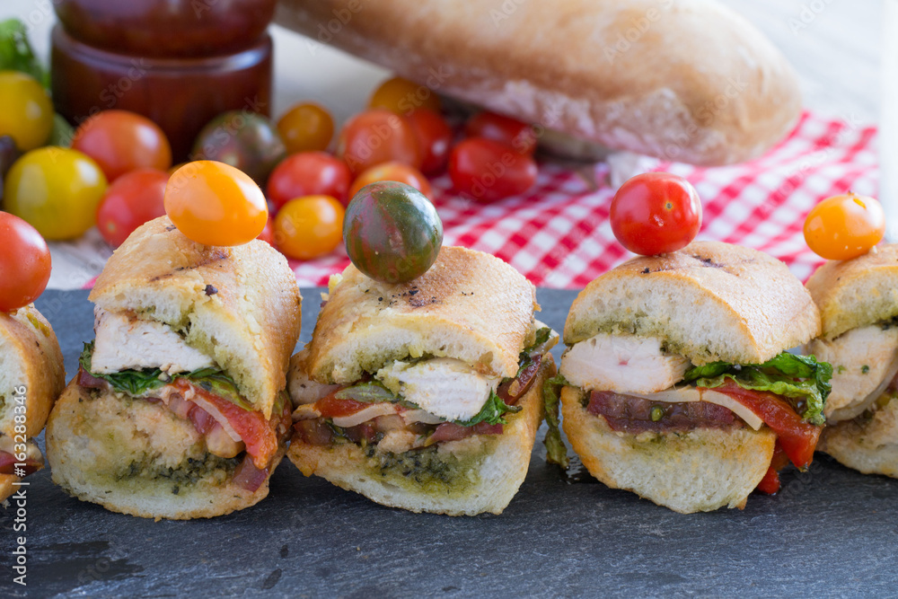 Grilled deli style chicken sandwiches sliced and topped with a cherry tomato Grilled deli style chicken sandwiches sliced and topped with a cherry tomato