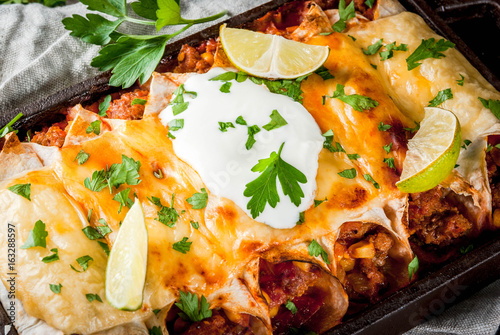 Mexican food. Cuisine of South America. Traditional dish of spicy beef enchiladas with corn, beans, tomato. On a baking tray, on old rustic wooden background. Close view