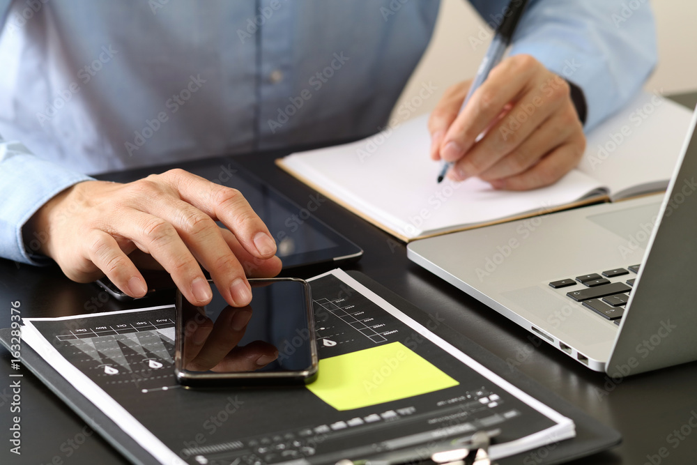 close up of businessman working with smart phone and digital tablet and laptop computer on wooden desk in modern office close up of businessman working with smart phone and digital tablet and laptop computer on wooden desk in modern office