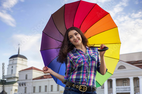She is holding a colorful umbrella. Beautiful Caucasian girl. In his hand a colorful umbrella. Maybe it will rain.
