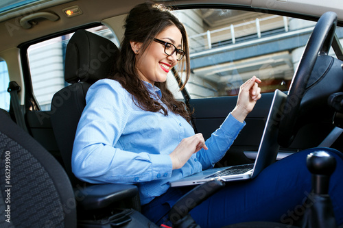 Beautiful young business woman sitting in the car working on laptop. © Zoran Zeremski