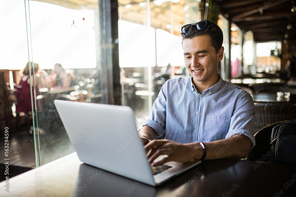 Portrait of handsome asian smiling man using laptop in the cafe Portrait of handsome asian smiling man using laptop in the cafe