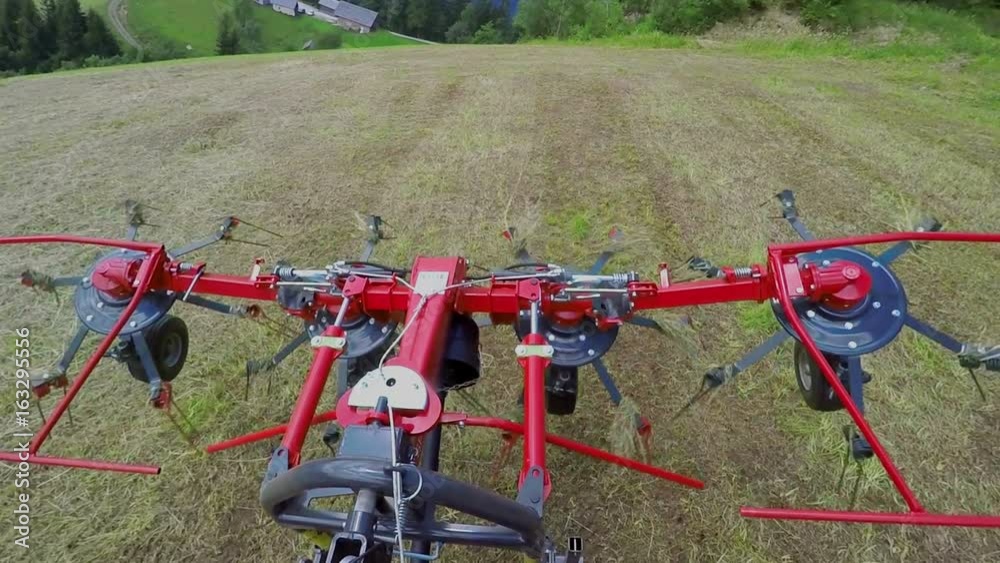 Rotary rakes are moving and the tractor is driving slowly on a big field with hay. Rotary rakes are moving and the tractor is driving slowly on a big field with hay.