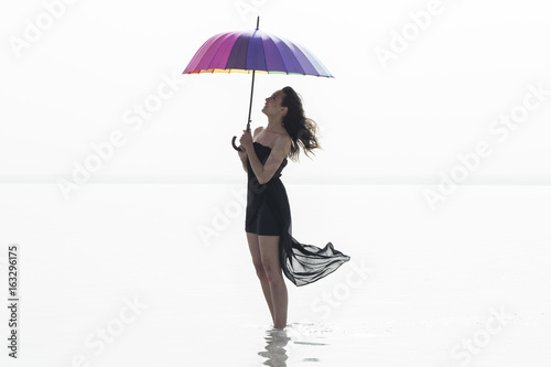 Woman holding colorful umbrella and walking on the salt lake. Sunrise sea and woman with umbrella in hand 