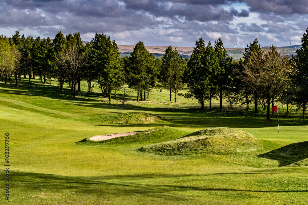 Obraz premium Golf Course on Springtime, Green golf field with trees and blue cloudy sky in background, England, UK