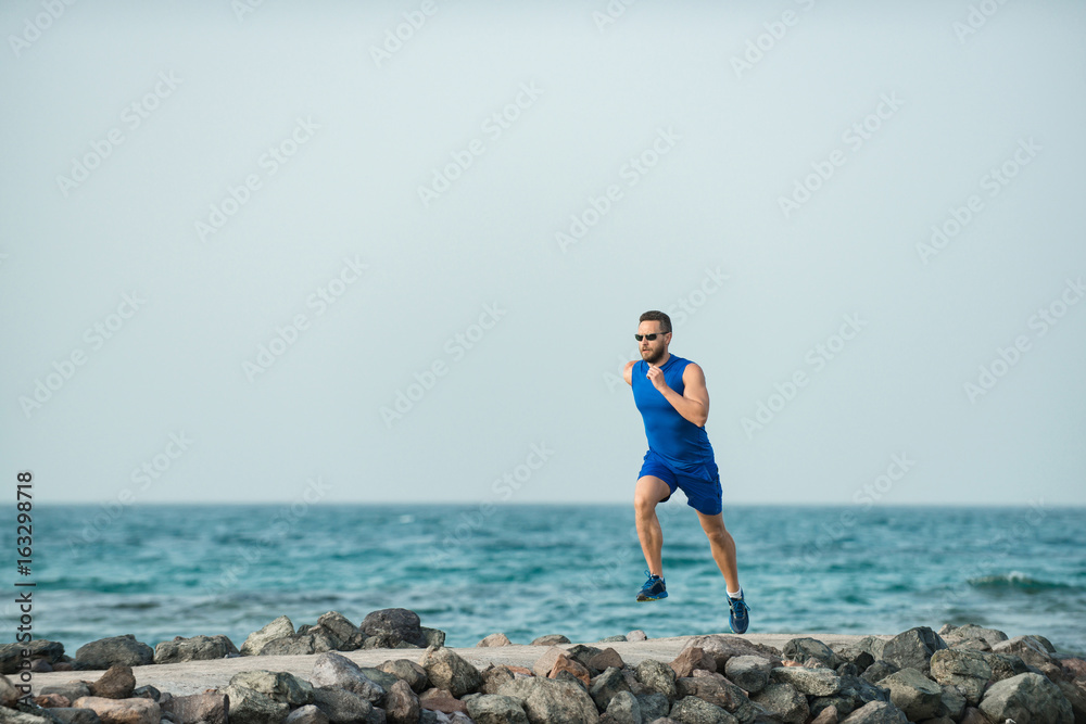 Man runner with handsome face running along stone coast