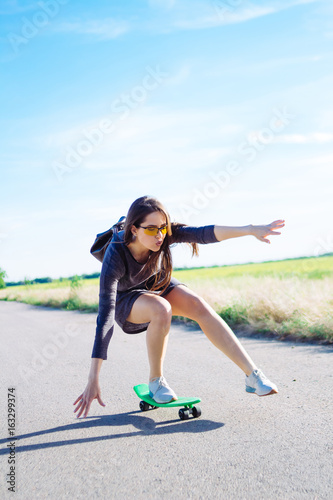Beautiful stylish girl in a dress rides a penny board, a light board, on the road outside the city © annaazary