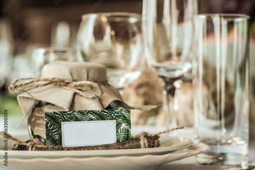 Rustic table setting for a wedding celebration in nice cozy restaurant. Wineglasses, plates and food on a table. Guests complement in a rustic jar. Nice card with a space for text Rustic table setting for a wedding celebration in nice cozy restaurant. Wineglasses, plates and food on a table. Guests complement in a rustic jar. Nice card with a space for text