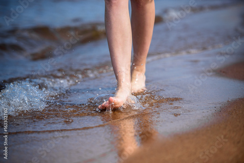  girl's legs are walking along the seashore in the water.
