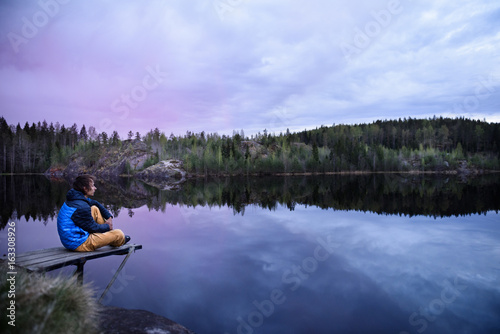 Man sitting on a pier at mountain lake, looking at beautiful at sunset. Scandinavia travel destination.