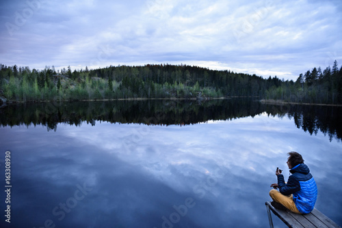 Young man sitting on a lake shore, smoking pipe. Scandinavia.