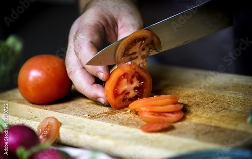 Closeup of hand with knife cutting fresh vegetable tomato