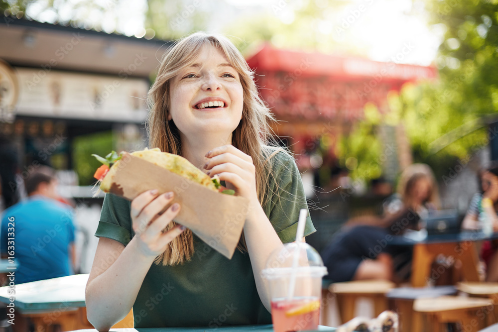 Girl eating taco. Hungry freckled blonde woman holding junk food on a ...