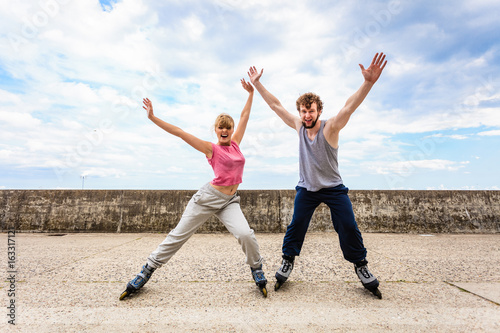 Two people on rollerblades with spread arms.