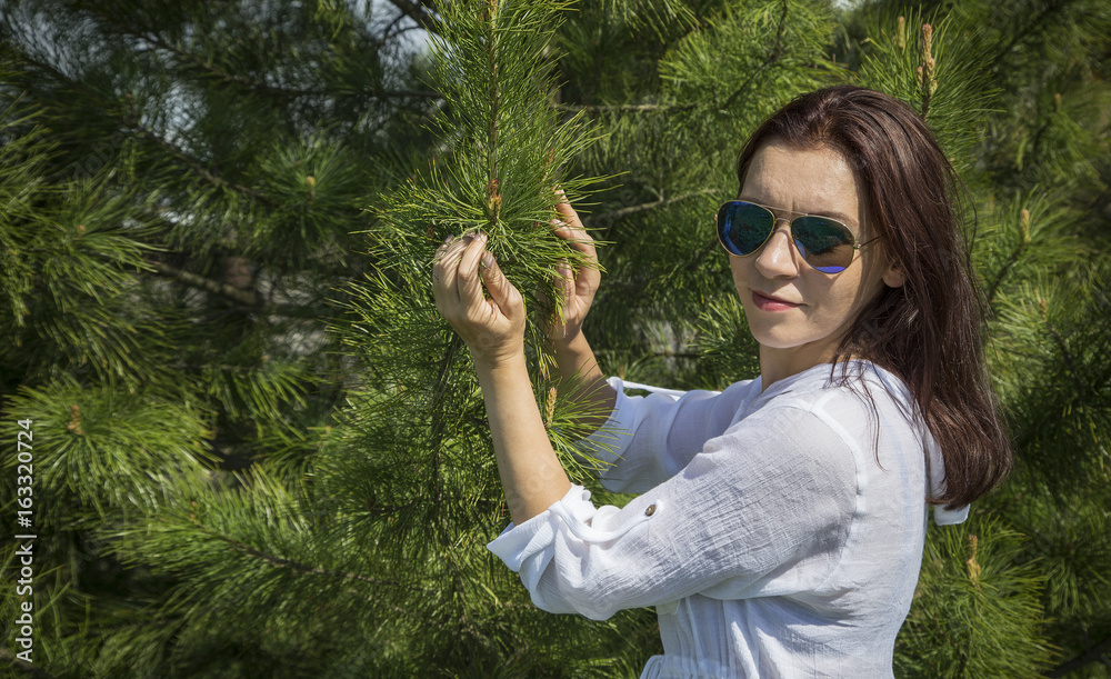 A woman in sunglasses stands near the cedar. A woman in sunglasses stands near the cedar.