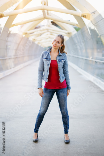 Portrait of beautiful smiling white Caucasian girl woman with pony tail, wearing jeans jacket outside in evening night city street bridge, looking in camera, lifestyle portrait concept