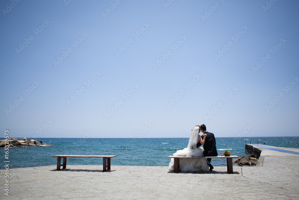 Couple smiling and embracing near wedding arch on beach. Honeymoon on sea or ocean