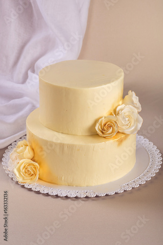 Beige 2 tiered wedding cake decorated with mastic roses stands on fabric background