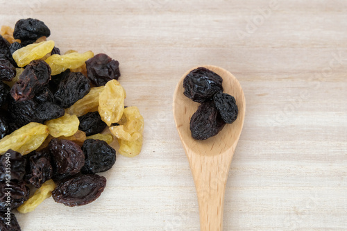 Dried raisins in wooden spoon on wood table.