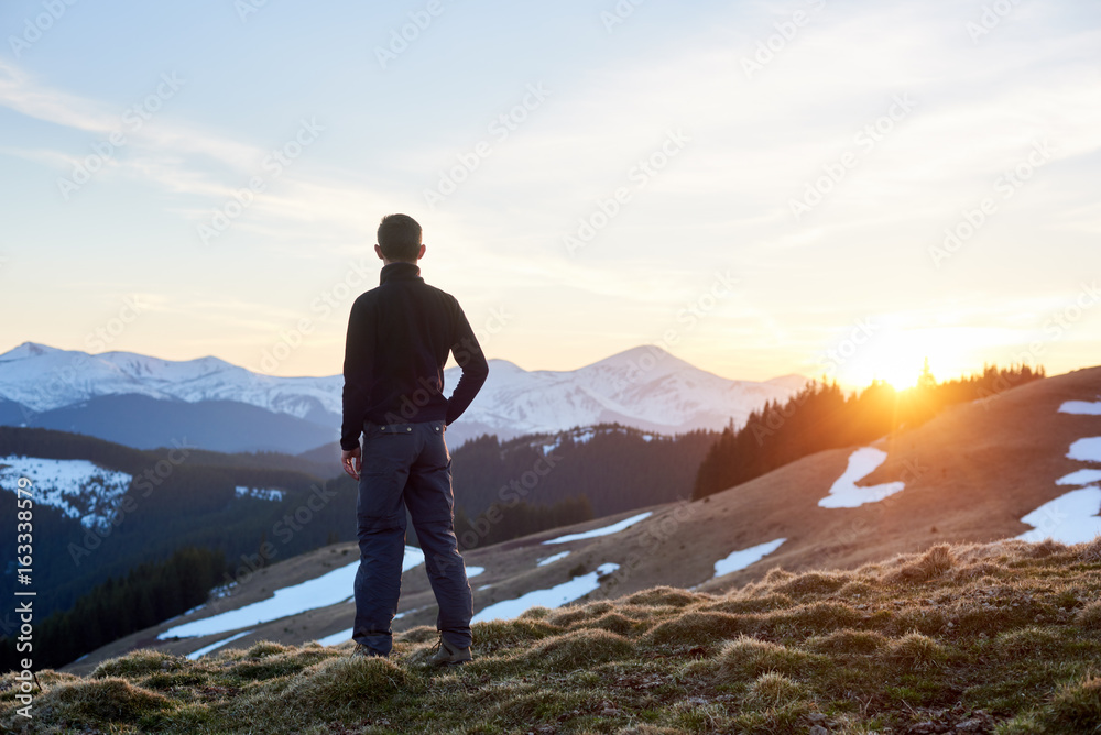 Rear view of male hiker watching wonderful scenery in mountains during spring colorful sunset