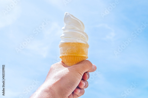 Soft white cream milk ice cream cone serve in hot summer day on sky background