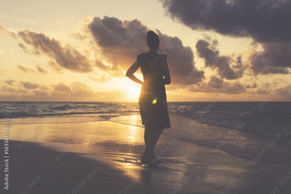 Female standing on the beach watching sunset. Travel lifestyle background