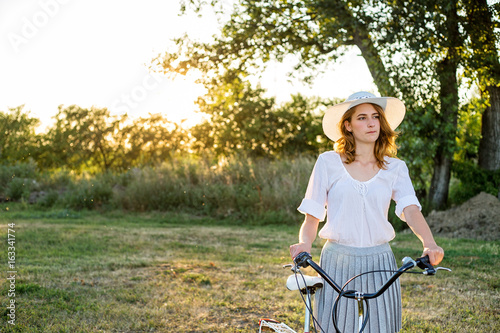 Beautiful young caucasian woman with a bicycle in park at summer sunny day