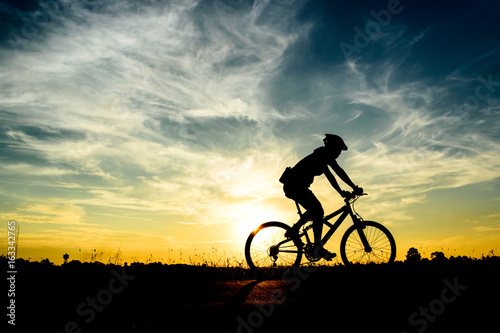 Silhouette of cyclist riding on bike at sunset.