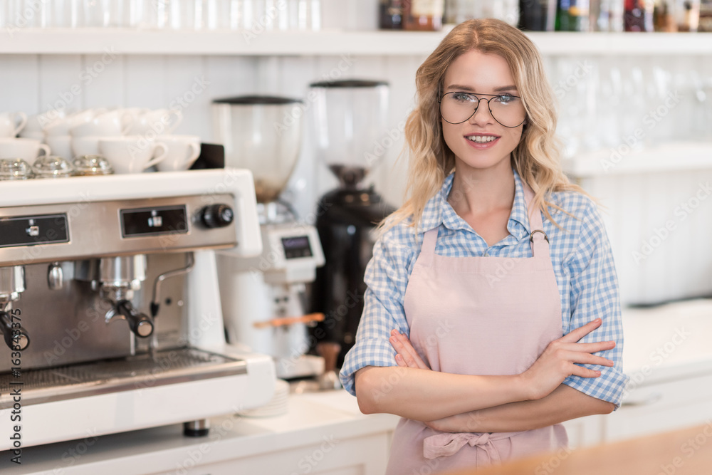 young smiling barista standing during work near coffee machine young smiling barista standing during work near coffee machine