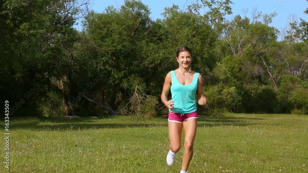 Pretty sporty woman jogging on a forest trail with headphones. Young fitness girl runner running on trail. Pretty sporty woman jogging on a forest trail with headphones. Young fitness girl runner running on trail.