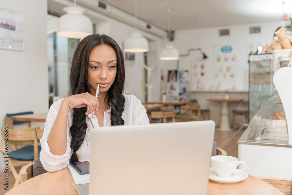 young pensive african american businesswoman using laptop while sitting at cafe young pensive african american businesswoman using laptop while sitting at cafe