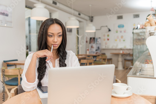 young pensive african american businesswoman using laptop while sitting at cafe