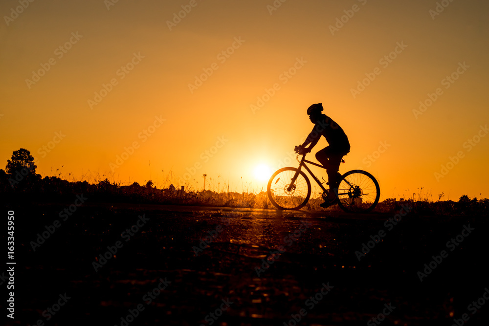 Silhouette of cyclist riding on a bike on road at sunset.