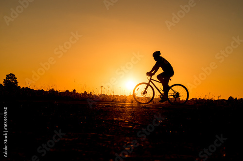 Silhouette of cyclist riding on a bike on road at sunset.