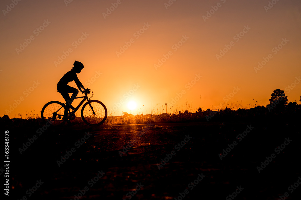 Fototapeta premium Silhouette of cyclist riding on a bike on road at sunset.