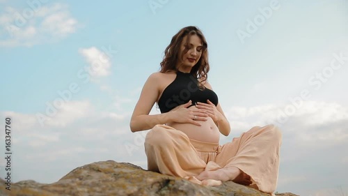 Pregnant caucasian woman doing sport outdoors. She breathes deeply and touch her belly, photo