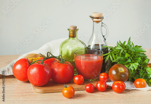 Tomatoes, tomato juice, parsley and bottles on a wooden table.