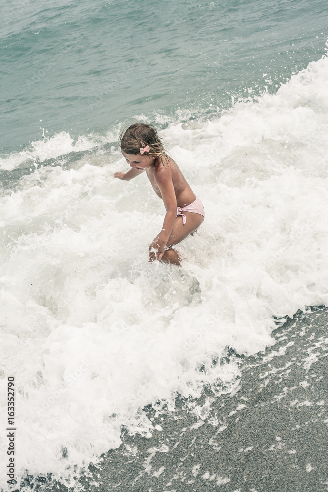 Girl enjoying the summer on the beach , playing in beautiful blue sea. Child playing on the waves.